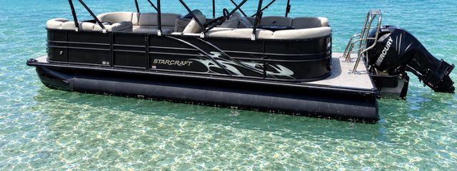 Black pontoon boat floating in clear turquoise water at the sandbar